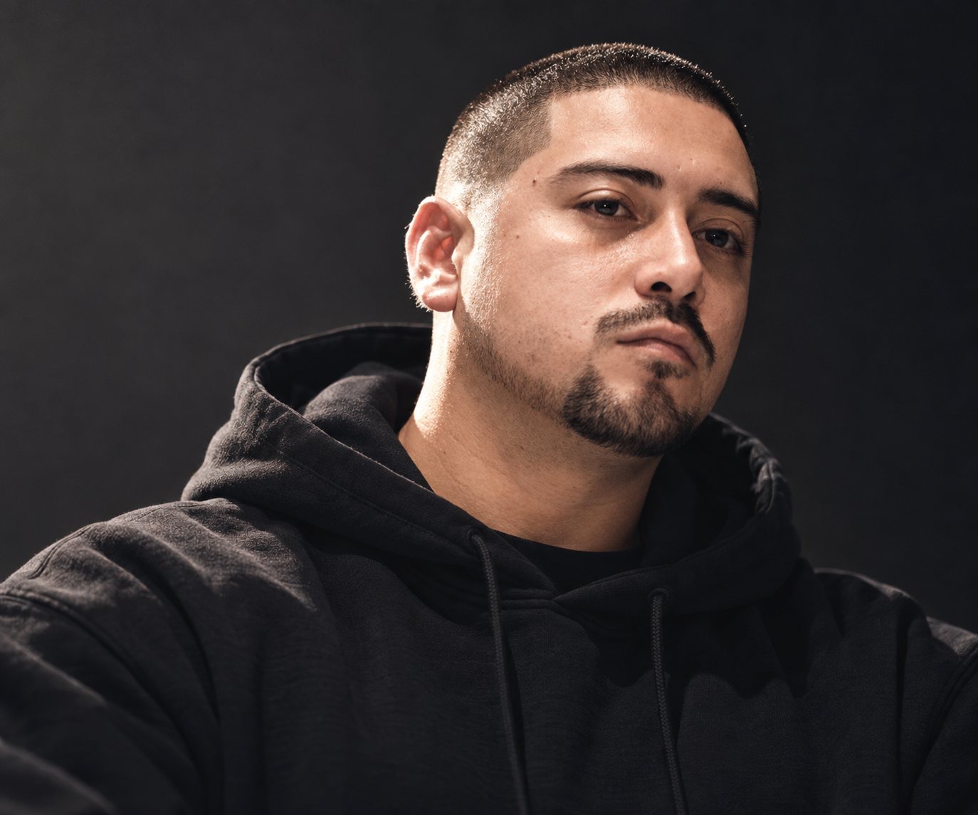 Portrait of Josue Bonilla in a black hoodie against a dark background